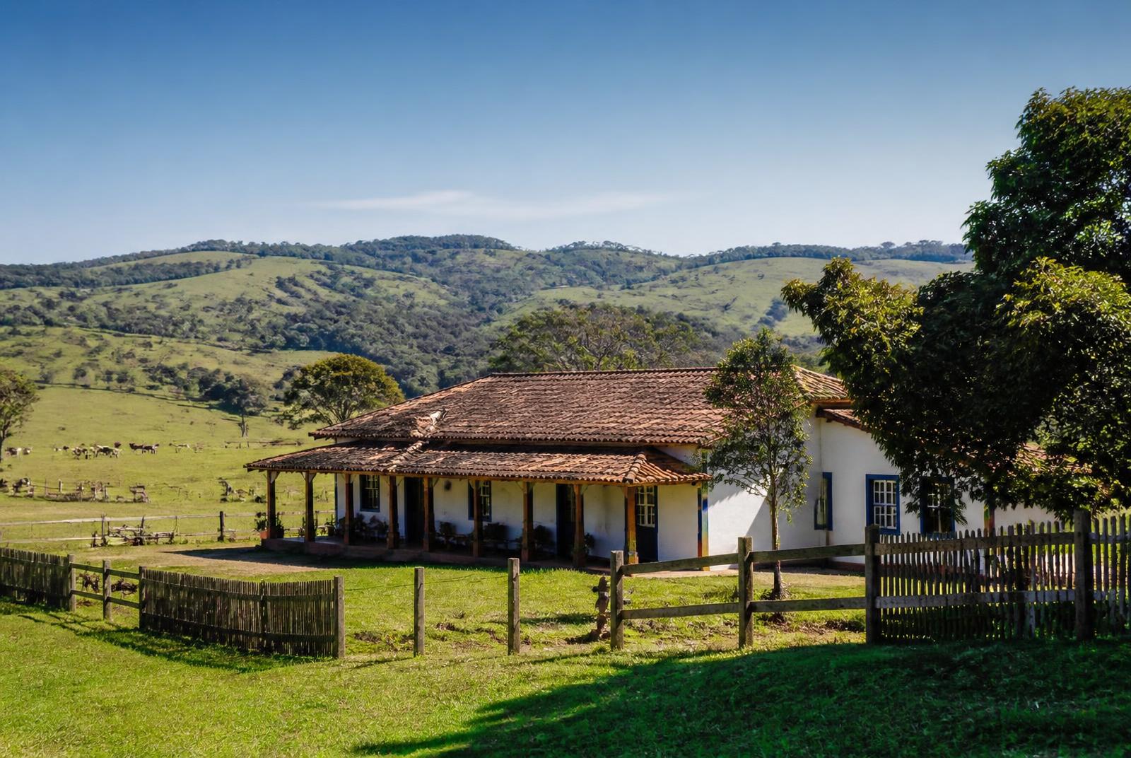 Sede de fazenda com varanda, pasto formado e morros ao fundo em Minas Gerais